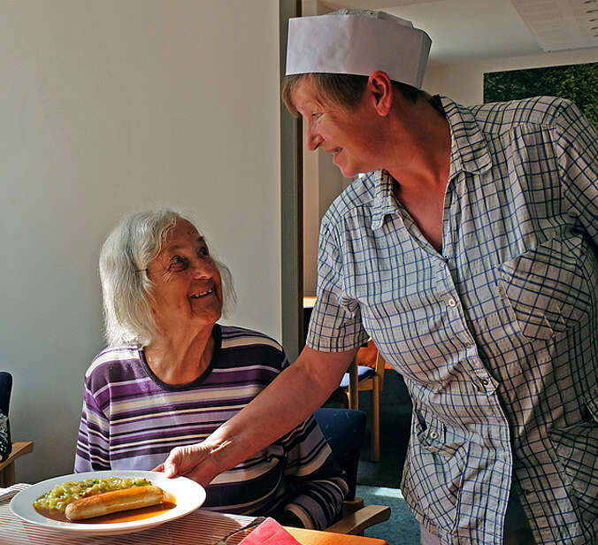 Frau bringt Seniorin essen an Tisch