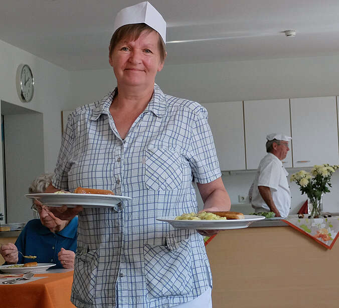 Frau steht im Speisesaal hält zwei Teller in den Händen