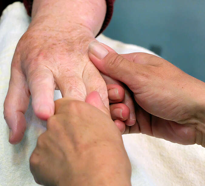 Pflegerin cremt Hände von Seniorin ein
