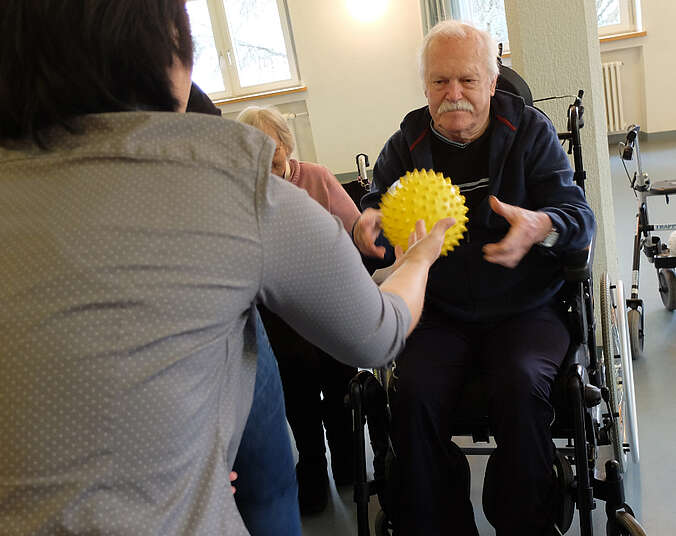 Frau wirft Senior in Rollstuhl einen Igelball zu